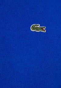 Logo de crocodile vert brodé sur fond de tissu tricoté bleu.