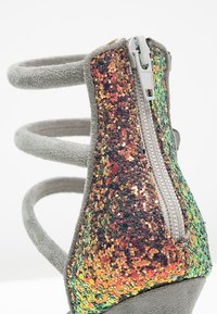 Sandale en daim gris avec trois brides et une fermeture éclair à l'arrière sur un contrefort de talon à paillettes multicolores.