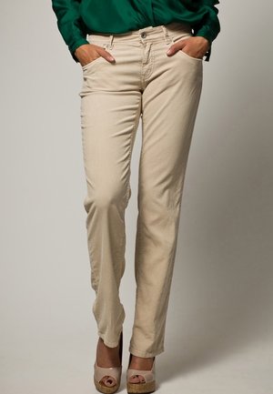 Jeans en coton beige avec une coupe droite, dotés de poches avant et d'une fermeture à bouton, associés à des chaussures à plateforme beiges.