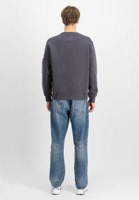 Szürke pulóver, bordás mandzsettákkal és szegéllyel, bal karján egy foltvarrott zsebbel, lazán szabott világoskék farmerrel párosítva.