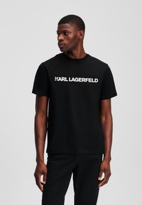 Juodas medvilnės marškinėliai su balta "KARL LAGERFELD" logotipu krūtinės srityje. Trumpomis rankovėmis ir apvaliu iškirpimu. Paprastas, tiesus kirpimas.