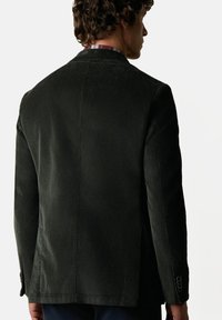 Ciemnozielona marynarka z korduroyu o strukturalnym kroju, z wentylowanym tyłem, klapami notch oraz guzikami na rękawach.