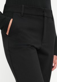 Čierne elegantné nohavice so hladkým materiálom, bočnými vreckami a priliehavým strihom. Pás je plochý bez viditeľných kovových prvkov.