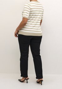 Suéter a rayas en crema y beige, con mangas cortas y un diseño ajustado, combinado con pantalones negros y zapatos de tacón negros.