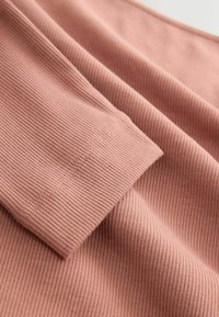 Ribbed fabric in a soft, dusty rose color. Features smooth seams and a textured surface, highlighting the material's stretch and flexibility.