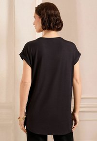 Top corto nero a maniche corte con una vestibilità comoda, scollatura rotonda e orli arrotolati. Tessuto morbido, orlo leggermente curvo sul retro.