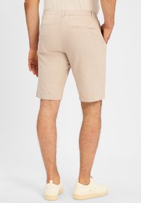 Light beige shorts made of textured fabric, featuring side and back pockets, and a straight cut, paired with white sneakers.