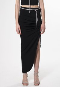Falda negra con fruncidos y una abertura lateral, con cintura ajustable decorada con detalles metálicos. Combinada con tacones altos plateados y con tiras.