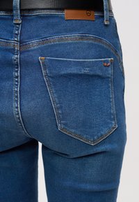 Λεπτομέρεια προσώπου που φοράει μπλε τζιν με πίσω τσέπη και ορατή καφέ δερμάτινη ετικέτα ζώνης.