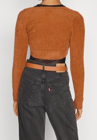 Osoba nosząca krótki, puszysty sweter w kolorze rdzawo-pomarańczowym, pod spodem przezroczysta czarna bluzka, czarne dżinsy Levi's z wysokim stanem oraz brązowy skórzany pasek.