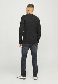 Zwart gestructureerd gebreid sweater gedragen met donkerdenim jeans en witte sneakers, met een ontspannen pasvorm en geribbelde details op de sweater.