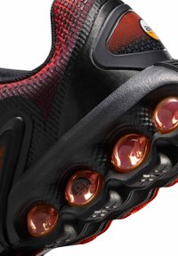 Primer plano de la suela de una zapatilla deportiva negra y roja con cuatro unidades de amortiguación de aire redondas naranjas visibles, etiquetadas como "Dn air".