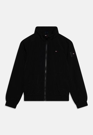 Giacca nera con zip, collo alto, polsini elastici, tasche laterali e piccoli loghi rossi, bianchi e blu sul petto e sulla manica sinistra.