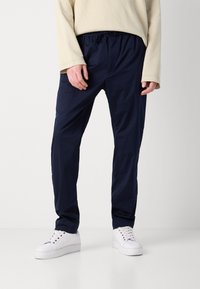 Marineblå, letvægtsbukser med elastisk talje og snoretræk, med sidelommer og en glat tekstur. Bæres med hvide sneakers.
