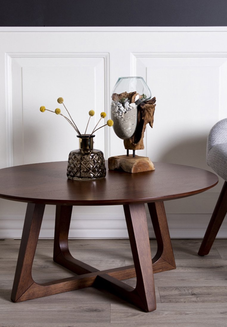 Tavolino da caffè rotondo in legno con un vaso decorativo in vetro marrone che contiene fiori gialli di billy ball e un terrario in vetro con pietre su un supporto in legno.