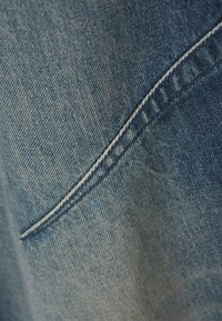 Lähellä oleva sininen farkkukangas, jossa on vino sauma valkoisella ompelella ja näkyvä kudontakuvio.