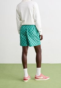 Turkosa rutiga shorts med elastisk midja, kombinerat med rosa sneakers och vita strumpor. Minimalistisk vit långärmad tröja.