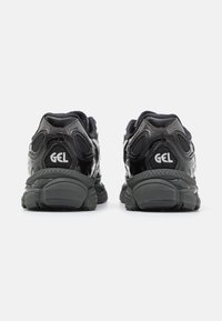 Dvojice černých sportovních bot s tlustými podrážkami a vyšitým nápisem "GEL" na patě, zobrazená zezadu na bílém pozadí.