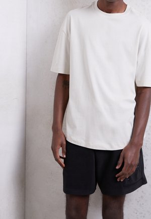 Lichtbeige katoenen t-shirt met korte mouwen, ronde hals en een relaxte pasvorm, gecombineerd met zwarte shorts met zijzakken.