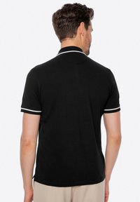 Černé polo tričko s texturovaným materiálem, s bílými pruhy na límci a rukávech, v klasickém střihu.