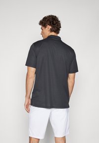 Dark gray polo shirt made of smooth fabric, with a classic collar and short sleeves, paired with white shorts. Worn from a rear view.
