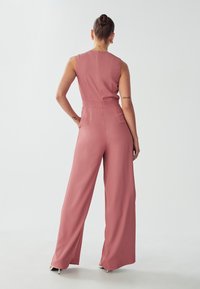 Roze, mouwloze jumpsuit met een getailleerde bovenkant en een ontwerp met wijde pijpen, voorzien van een rits aan de achterkant en een strakke silhouet. Soepele stofstructuur.