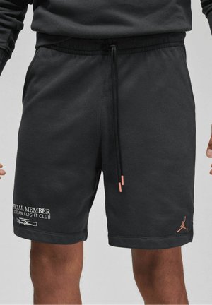 Czarne spodenki Jordan z sznurkiem, z napisem „Official Member Jordan Flight Club” na lewej nodze i logo Jumpman na prawej nodze, noszone przez osobę.