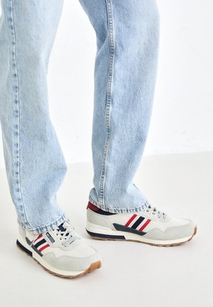 Svjetlosive sportske cipele s teksturiranom površinom, naglašene crvenim i mornarsko plavim prugama. Uparene s plavim trakom ravnog kroja, s poderanim rubovima.