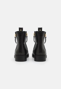 Bottes courtes en cuir noir avec une texture lisse, des accents en métal doré, un bout arrondi et deux fermetures éclair latérales pour un enfilage facile.