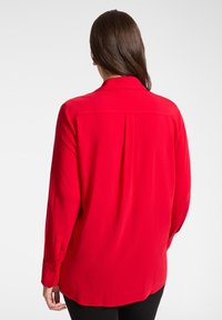 Czerwona bluzka z długim rękawem wykonana z gładkiej tkaniny, z plisą z tyłu, klasycznym kołnierzem i mankietami na guziki.