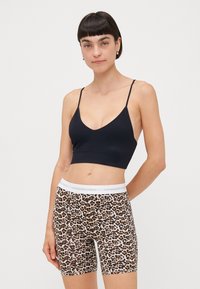 Svart ribbet bralette med tynne stropper, kombinert med leopardmønstrede sykkelshorts med hvit midjebånd med logo.