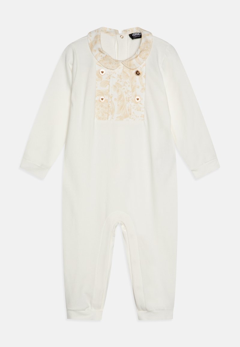 Bílý overal s dlouhými rukávy, který má texturovanou vzorovanou část v jemné béžové barvě a dekorativní zlaté knoflíky na prsou.
