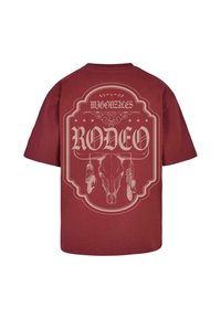 Maroon cotton t-shirt featuring a large, light-colored printed graphic of a skull and feathers with the word "RODEO" prominently displayed.
