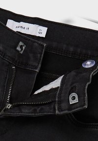 Pantaloni in denim nero con patta zip, chiusura a bottone e foderatura in tessuto bianco. L'etichetta recita "name it by 128."
