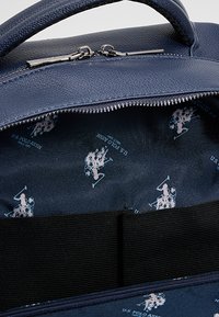 Sinisen nahkalaukun sisäpuoli, jossa on sileä pinta, toistuva valkoinen Polo-logokuvio ja musta joustava nauha järjestelyä varten.