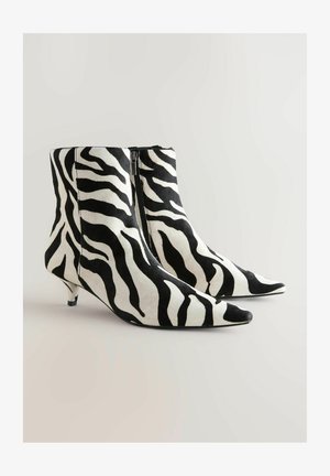 Czarno-białe botki na kostkę w wzór zebry, z ostrym noskiem i niskim obcasem typu koci pazur, z zamkiem błyskawicznym z boku i gładką fakturą.