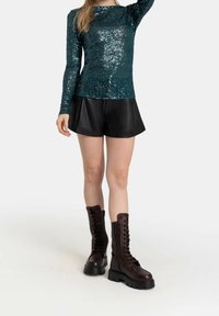 Ett turkosa paljett-topp med långa ärmar i kombination med svarta lädershorts och bruna snörstövlar som når anklarna. Stövlarna har tjocka sulor och en sidodedragkedja.