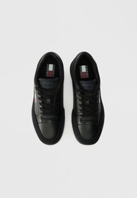 Μαύρα αθλητικά παπούτσια με επάνω μέρος από λείο δέρμα, σχέδιο με κορδόνια, τρυπητή μύτη και διακριτικά λογότυπα στη γλώσσα και στο πλάι.