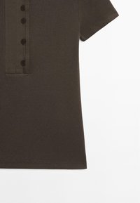 Polo shirt a coste marrone scuro con chiusura a bottoni, maniche corte e finitura testurizzata. Tessuto liscio con design casual.