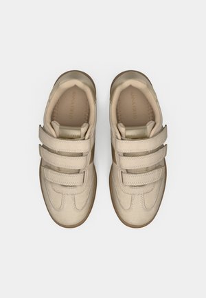 Para beżowych sneakersów z trzema rzepami, wyściełanymi kołnierzami i brązowymi podeszwami, widzianych z góry na białym tle.