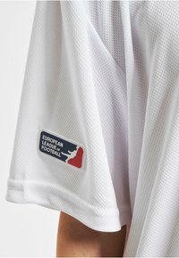 Biała siatkowa koszulka piłkarska z wyraźną aplikacją logo Europejskiej Ligi Futbolowej na rękawie.