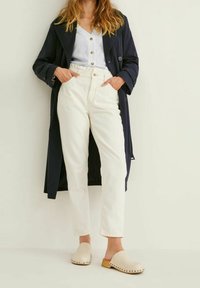 Navy trench coat, white button-up shirt, cream high-waisted trousers, and beige clogs with wood accents. Smooth fabrics, relaxed fit.