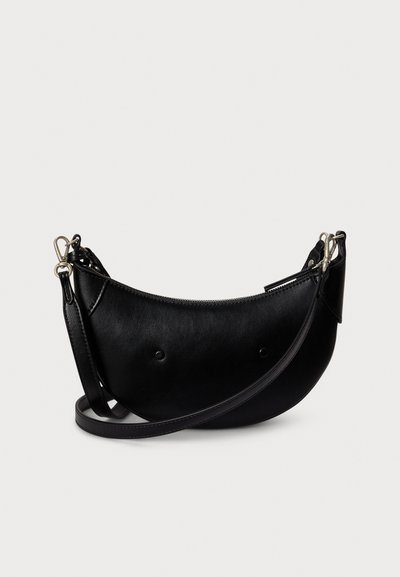 Czarna skórzana torebka o zaokrąglonym kształcie, zamykana na zamek błyskawiczny, z regulowanym paskiem. Na przodzie ozdobiona zaokrąglonymi ćwiekami dla dodatkowego detalu.