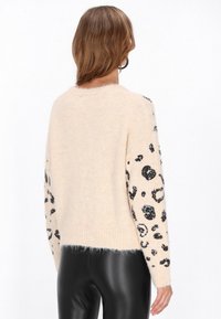 Jasno be�żowy sweter wykonany z miękkiego materiału, z czarnym cekinowym wzorem w panterkę na rękawach. Ribbed cuffs i dół, luźny krój.