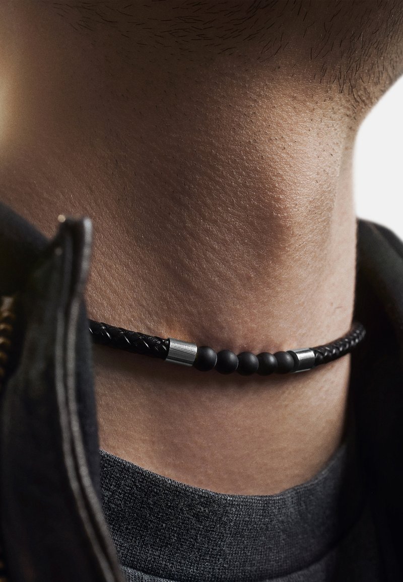 Sort vævet læder choker halskæde med matte perler og sølv accenter, der har en glat tekstur og en tætsiddende pasform omkring halsen.