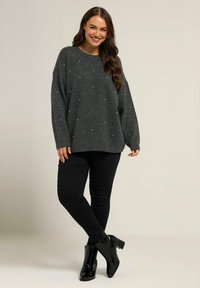 Maglione grigio a maglia con perle decorative, vestibilità comoda e spalle scese, abbinato a pantaloni neri attillati e stivaletti lucidi.