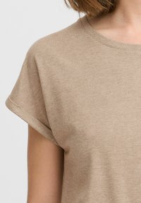 T-shirt beige a maniche corte, con collo rotondo, realizzato in tessuto morbido con una finitura leggermente testurizzata e manicotti delle maniche arrotolati.