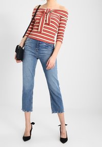 Rød og beige stribet off-the-shoulder top med en sløjfedetalje, parret med cropped jeans med fransk kant i blå og sorte spidse højhælede sko.