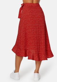 Falda roja hasta la rodilla con un dobladillo acampanado, patrón floral blanco y un detalle de cinturilla atada. Combinada con zapatillas blancas.