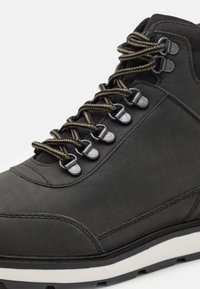 Bota de senderismo negra ligera con parte superior de cuero texturizado,cordones verdes contrastantes y suela de goma blanca. Ojales reforzados que añaden durabilidad.